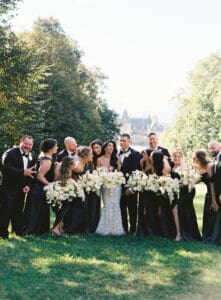Biltmore Weddings – Marcos and Gaby Bride and groom surrounded by bridesmaids in black dresses and groomsmen in tuxedos holding white bouquets.