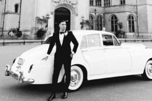 Biltmore Weddings – Marcos and Gaby Black and white portrait of groom in tuxedo leaning on classic white car in front of the Biltmore Estate.
