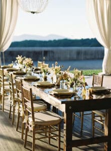 Biltmore Weddings – Marcos and Gaby Long wooden table with gold chairs, floral centerpieces, and place settings overlooking the Blue Ridge Mountains.