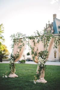 Biltmore Weddings – Marcos and Gaby Romantic draped arch with greenery and white flowers on the Biltmore Estate lawn.
