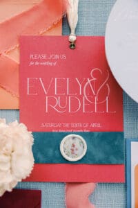 Wedding by Terran Ward Events Flat lay of wedding invitation on a textured light blue background with other items that compliment the red and blue of the invitation. Wedding planned by luxury Asheville wedding planner Terran Ward