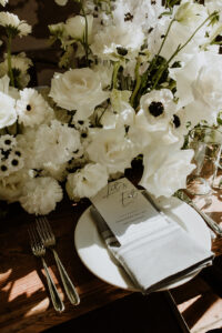 Rhubarb Asheville Wedding Planned by Terran Ward Close-up of a guest's spot at a rustic-styled reception table featuring white florals, silverware, a white menu and plate, and a light green napkin. Wedding planned by Asheville wedding planner Terran Ward — bold editorial mountain wedding design.