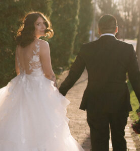 Grand Bohemian Asheville Wedding_Carly and David Back view of bride and groom walking down a brick pathway lined with greenery, as the bride looks towards the camera at the Grand Bohemian Asheville. Wedding Planned by luxury Asheville Planner Terran Ward