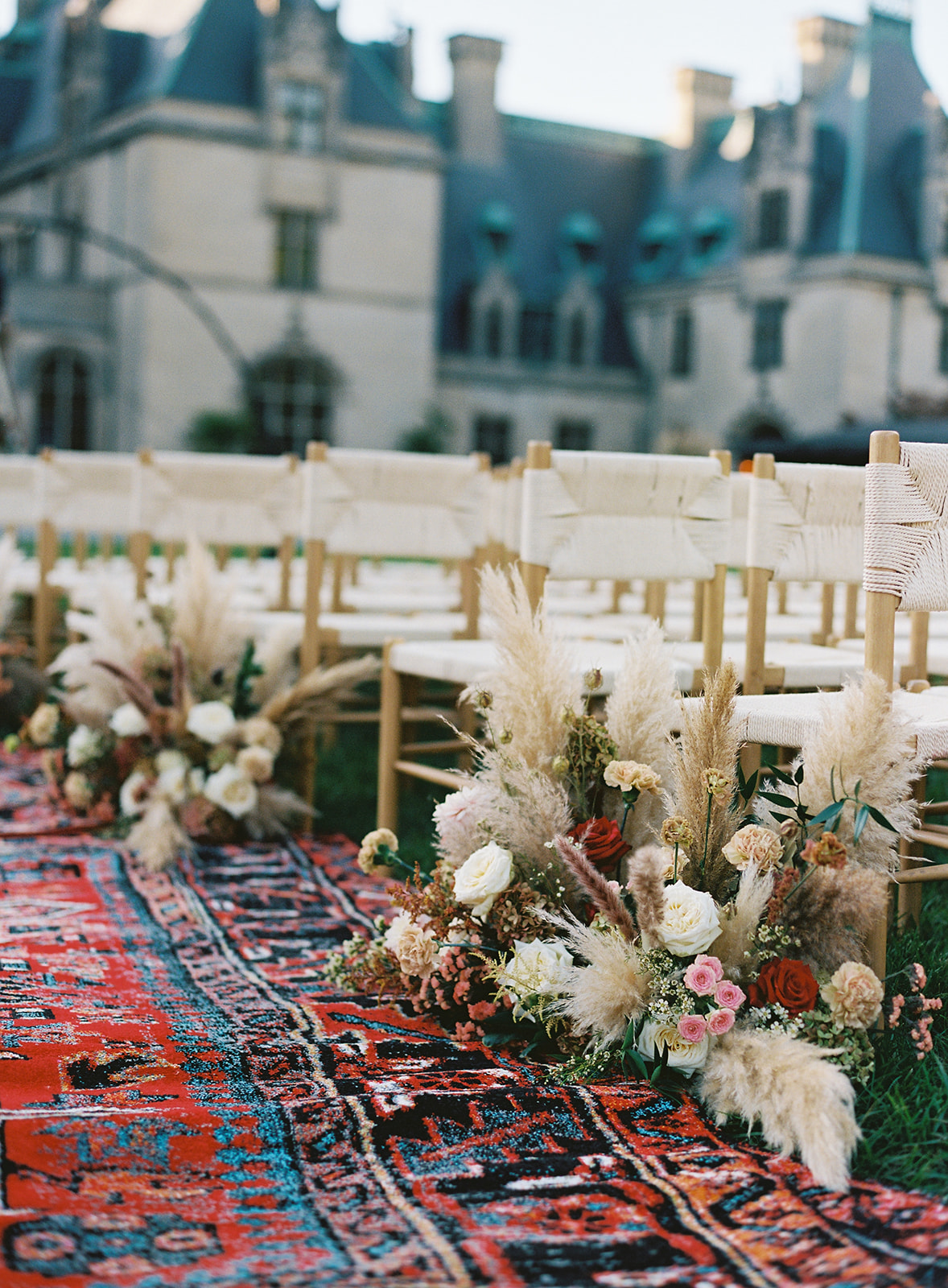 Close-up of Moroccan-inspired outdoor wedding aisle featuring florals, a colorful rug, and textured chairs outside the Biltmore Estate. Wedding planned by Asheville wedding planner Terran Ward — bold editorial mountain wedding design.