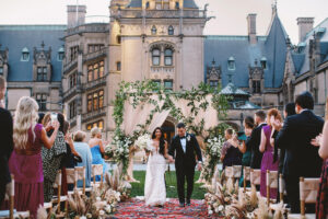 Biltmore Estate Asheville Wedding – Marcos and Gaby Bride and groom walking down the aisle after ceremony at Biltmore Estate as guests applaud. Wedding planned by Asheville wedding planner Terran Ward — bold editorial design setup.