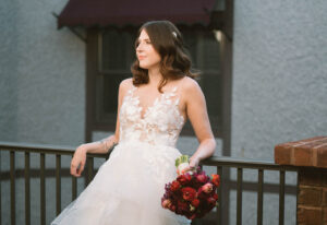 Grand Bohemian Asheville Wedding_Carly and David Close-up of bride leaning against railing with a red bouquet in her hand at the Grand Bohemian Asheville. Wedding Planned by luxury Asheville Planner Terran Ward