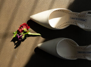 Grand Bohemian Asheville Wedding_Carly and David Close-up of white wedding heels and smell red wildflowers at the Grand Bohemian Asheville. Wedding Planned by luxury Asheville Planner Terran Ward