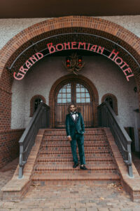 Daniela and Angelo Wedding Grand Bohemian Asheville Groom posing outside the Grand Bohemian Hotel entrance in green suit. Wedding Planned by Terran Ward at The Grand Bohemian Asheville