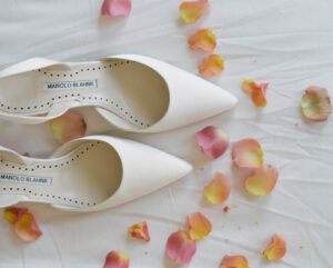Grand Bohemian Asheville Wedding_Carly and David Flat of white wedding heels on a white background with pink and orange flower petals at the Grand Bohemian Asheville. Wedding Planned by luxury Asheville Planner Terran Ward