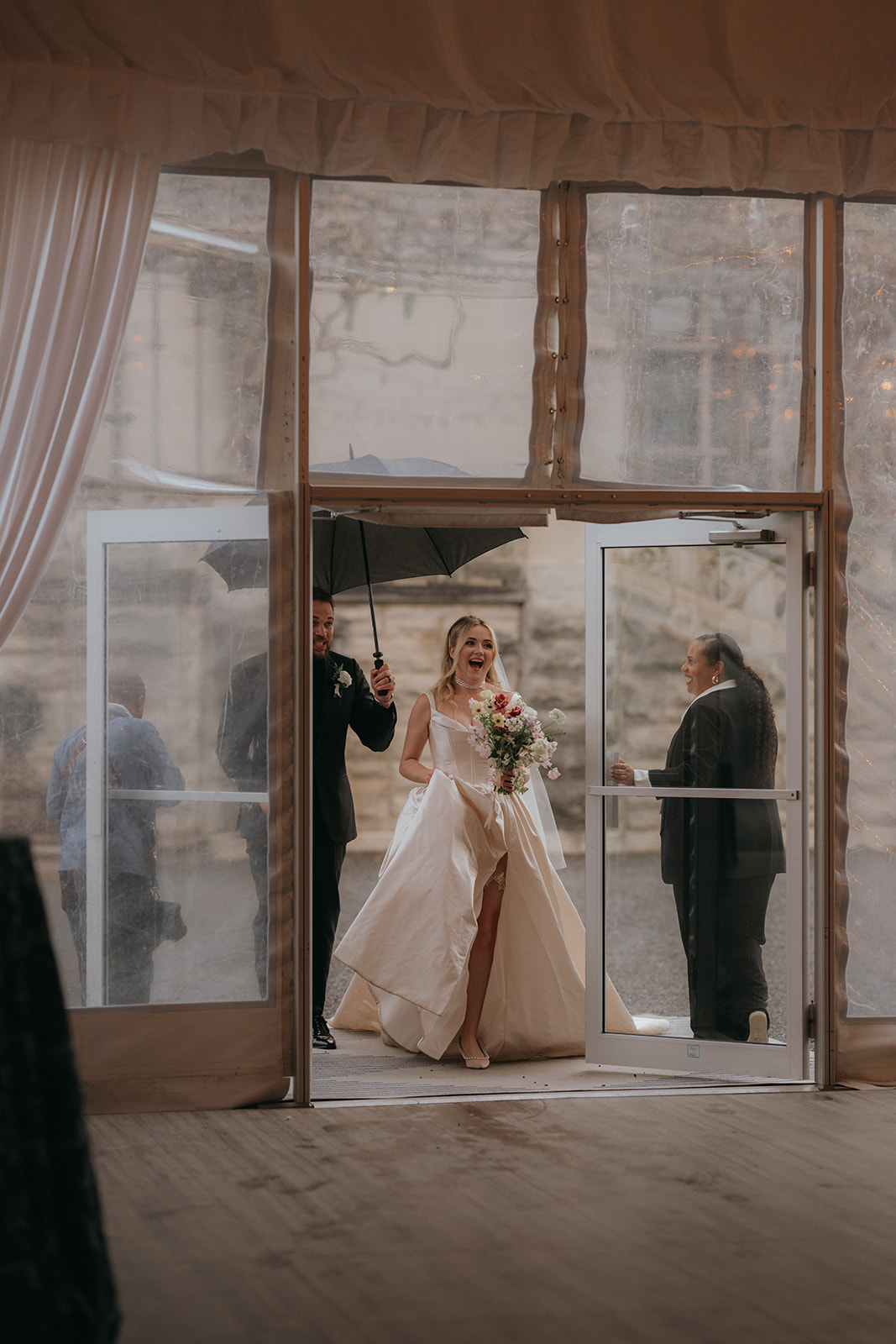 Bride and groom entering reception hall at Biltmore Estate. Groom holds umbrella for smiling bride. Wedding rain plan planned by Asheville wedding planner Terran Ward.