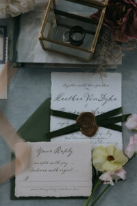 Biltmore Estate Asheville Wedding_Heather + Ben Flat lay of wedding invitation suite with wax seal, green ribbon, and florals at the Biltmore Estate. Wedding planned by Asheville wedding planner Terran Ward — bold editorial mountain wedding design.