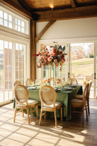 Mountain Wedding – Kaitlyn and Eric Shot of one wedding reception table with light wooden chairs, a green tablecloth, and a tall, fall floral centerpiece. Wedding planned by Asheville wedding planner Terran Ward — bold editorial design setup.