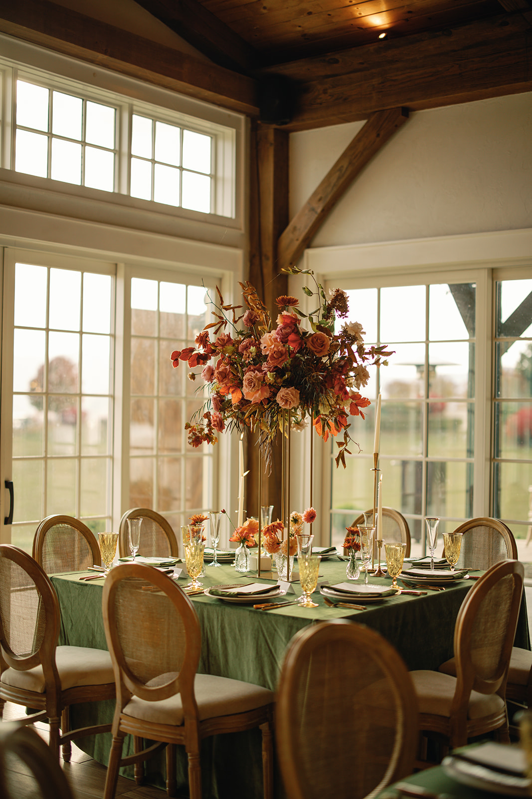 Close-up of one wedding reception table with light wooden chairs, a green tablecloth, and a tall, fall floral centerpiece. Wedding planned by Asheville wedding planner Terran Ward — bold editorial design setup.