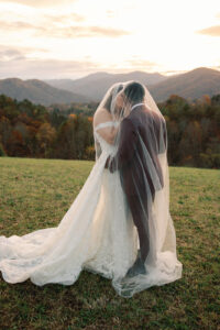 Mountain Wedding – Kaitlyn and Eric Bride and groom kissing under bride's veil outside with mountain views. Wedding planned by Asheville wedding planner Terran Ward — bold editorial design setup.