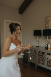 Chestnut Ridge Asheville Wedding_Mikaela + Jacob Bride holds two champagne glasses while smiling. Wedding planned by Asheville wedding planner Terran Ward — bold editorial mountain wedding design.