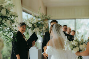 Chestnut Ridge Asheville Wedding_Mikaela + Jacob Bride and groom standing before officiant during ceremony surrounded by white florals at Chestnut Ridge. Wedding planned by Asheville wedding planner Terran Ward — bold editorial mountain wedding design.