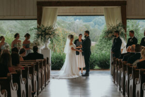Chestnut Ridge Asheville Wedding_Mikaela + Jacob Indoor wedding ceremony at Chestnut Ridge with mountain views framed by white drapery and floral urns. Wedding planned by Asheville wedding planner Terran Ward — bold editorial mountain wedding design.