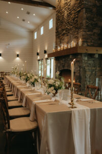 Chestnut Ridge Asheville Wedding_Mikaela + Jacob Long reception table with neutral linens, candles, and lush white floral arrangements inside Chestnut Ridge barn. Wedding planned by Asheville wedding planner Terran Ward — bold editorial mountain wedding design.