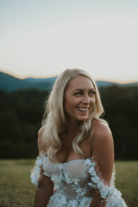 Bride looking to the side in a lace-floral, shoulder-less gown. Asheville wedding planner Terran Ward created sunset-driven timeline for mountain wedding
