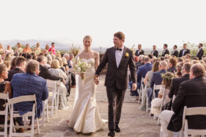 Omni Grove Park Inn Weddings – Mr. and Mrs. Kelly Bride and groom walk down the aisle of an outdoor ceremony at Omni Grove Park Inn, smiling and holding hands.