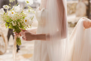 Omni Grove Park Inn Weddings – Mr. and Mrs. Kelly Bride holds a bouquet of white daisies and cosmos with the groom adjusting her dress at the Omni Grove Park Inn
