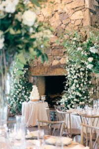 Omni Grove Park Inn Asheville Wedding_Ryan and Lauren Far away shot of a four-tier wedding cake with cascading white roses. White florals and delicate table design in the foreground. Wedding planned by Asheville wedding planner Terran Ward — bold editorial mountain wedding design.