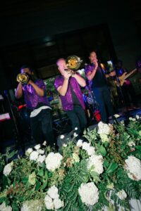 Grove Park Inn Asheville Wedding – Lauren and Ryan Live band, dressed in purple and black performs at a wedding, white flowers in front of them. Wedding planned by Asheville wedding planner Terran Ward — bold editorial design setup.