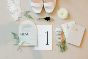 Bohemian Hotel Asheville Wedding_Toree and Brandon Flat lay with reception menu, lace halters, white shoes, a white flower, leaves, and ring boxes with rings. Wedding planned by Asheville wedding planner Terran Ward — bold editorial mountain wedding design.