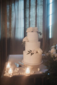 Daniela and Angelo Wedding Grand Bohemian Asheville Close-up of white 3-tiered cake featuring green leaves and white roses. Wedding Planned by Terran Ward at The Grand Bohemian Asheville