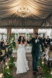 Daniela and Angelo Wedding Grand Bohemian Asheville Bride and groom walking down the aisle holding hands and smiling under tent with chandeliers. Guests cheer and clap. Wedding Planned by Terran Ward at The Grand Bohemian Asheville