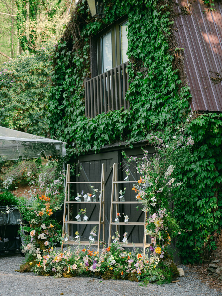 Shelving with plants on it in front of brown barn with vines at Hawkesdene. Wedding planned by Terran Ward