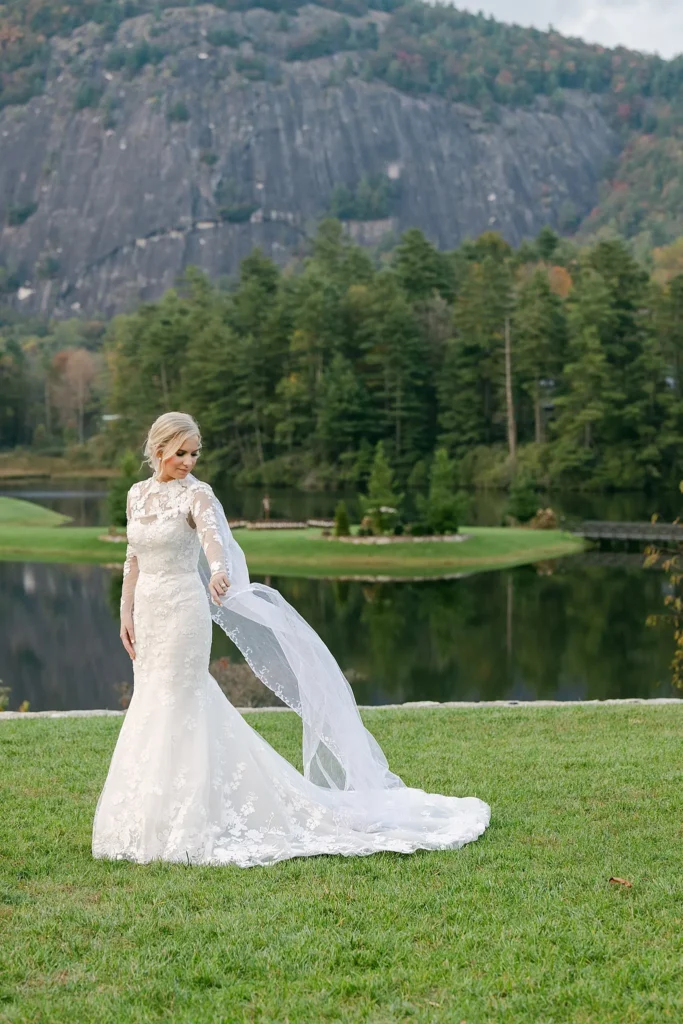Bride looking at her sleeve of her lace wedding gown in front of lake and mountain. Wedding planned by Terran Ward.