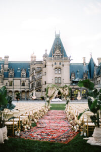 Wedding aisle lined with Persian rugs leading to floral arch at Biltmore Estate ceremony. Destination wedding in Asheville — Terran Ward planning mountain ceremony