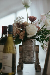 close-up of floral centerpiece featuring white, maroon, and pink flowers in a star wars vase. Bottles of wine sit next to it. Asheville wedding planner Terran Ward creating luxury weddings with a budget.