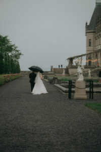 Back view of bride and groom walking under an umbrella outside the Biltmore Estate. Asheville wedding planner Terran Ward creating luxury weddings with a budget.