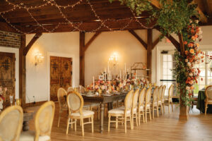 Wide view of long dark wood reception table featuring light colored chairs and fall florals. Asheville wedding planner Terran Ward creating luxury weddings with a budget.