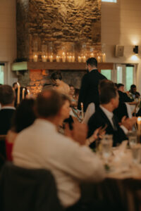 bride and groom standing in the Chestnut Ridge Reception room while guests, seated, clap and cheer. Destination wedding in Asheville — Terran Ward planning mountain ceremony
