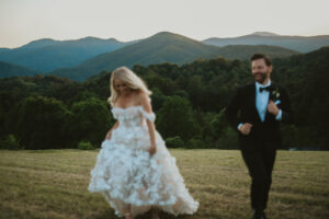 Blurry photo of bride and groom running across a field, smiling, with the Blue Ridge Mountains in the background. Asheville micro wedding — modern editorial setup by Terran Ward