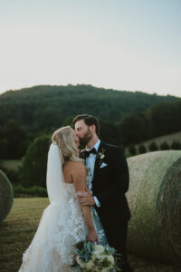 Bride and groom kissing next to a haybale on a field with the Blue Ridge Mountains in the background. Asheville micro wedding — modern editorial setup by Terran Ward