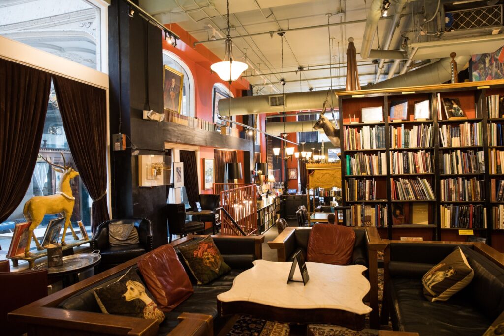 A sitting area in the Battery Park Book Exchange bar featuring rustic leather couches and a uniquely shaped table and bookshelves.