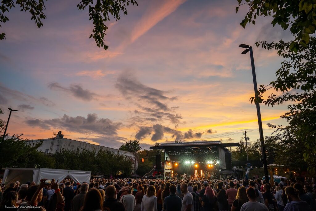 View of a concert at the Asheville Yards Amphitheater at sunset, featuring a large crowd.